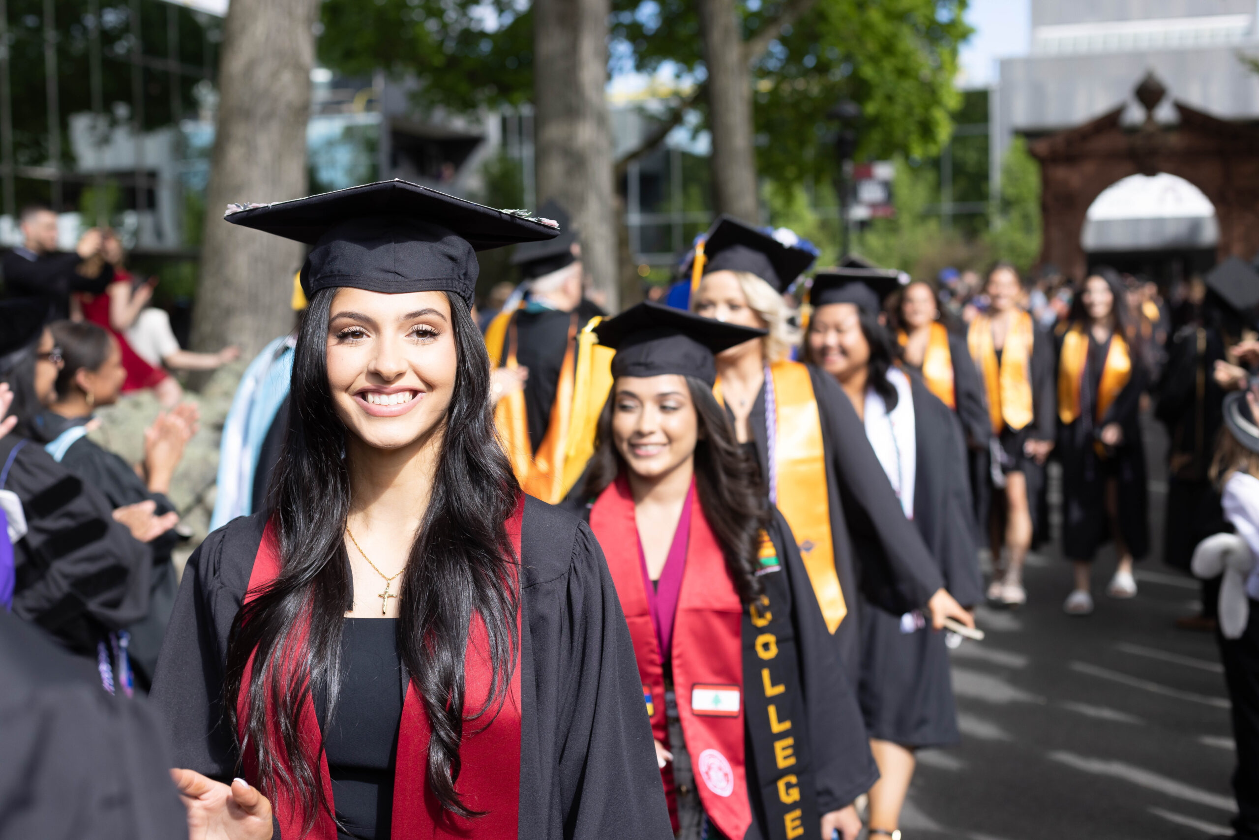 Graduating students in caps and gowns walking through Ramapo Arch