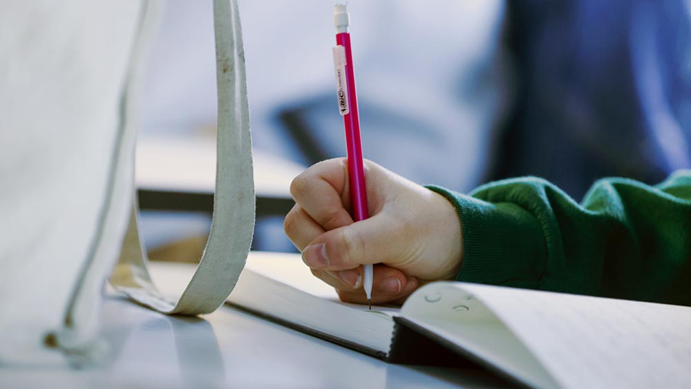 close up of a students hand writing with a pencil in a notebook