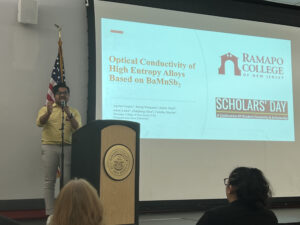 Student at podium presenting a powerpoint of their research entitled "Optical Conductiviity of High Entropy Alloys Based on BaMnSb2" on SCHOLARS' DAY, April 16th, 2024.