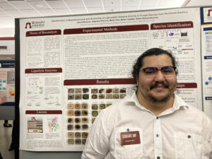 Student posing in front of their research poster on the identification of basidiomycetes and screening of ligninolytic enzyme activity in fungal species from Northeast America, SCHOLARS' DAY, April 16th, 2024.