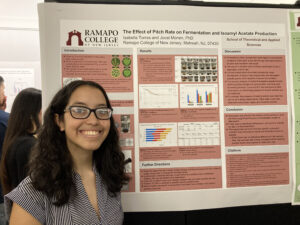 Student posing in front of their research poster on the effects of pitch rate on fermentation and isoamyl acetate production, SCHOLARS' DAY, April 16th, 2024.